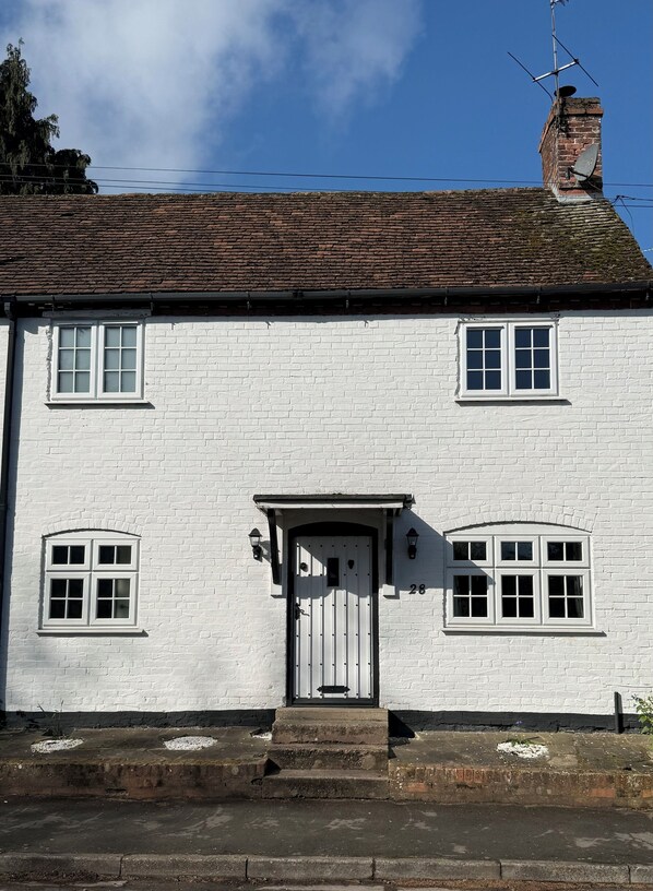 A white brick building with a white door, two windows on the upper floor, and a chimney.