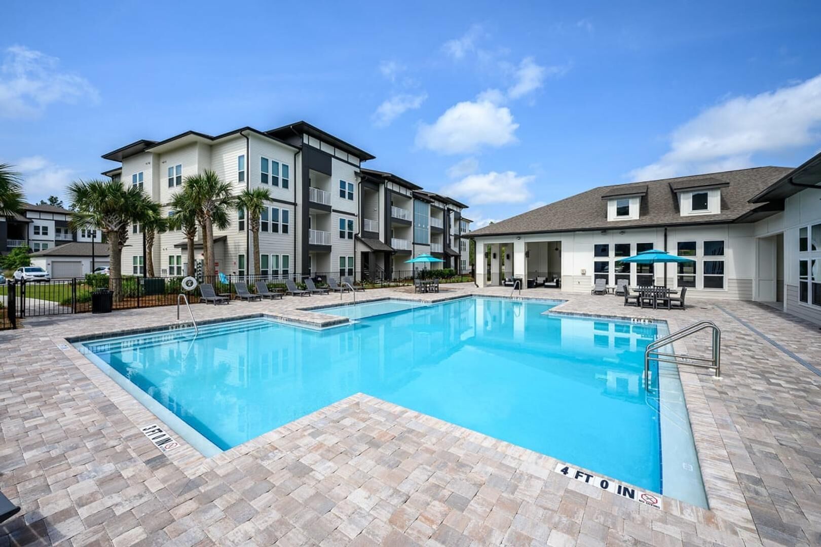 A swimming pool with a 4 ft 0 in depth marker, surrounded by a brick patio, and adjacent to a multi-story building with balconies.