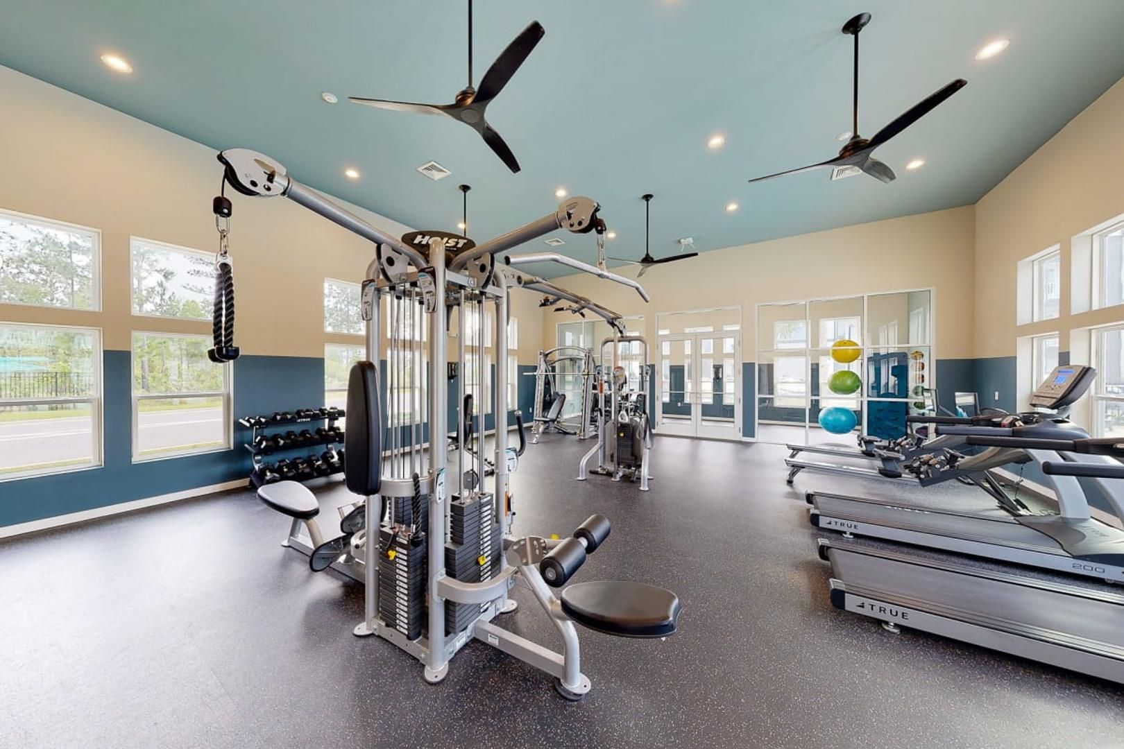 Ein Fitnessstudio mit Deckenventilatoren, Trainingsgeräten, Laufbändern und großen Fenstern.