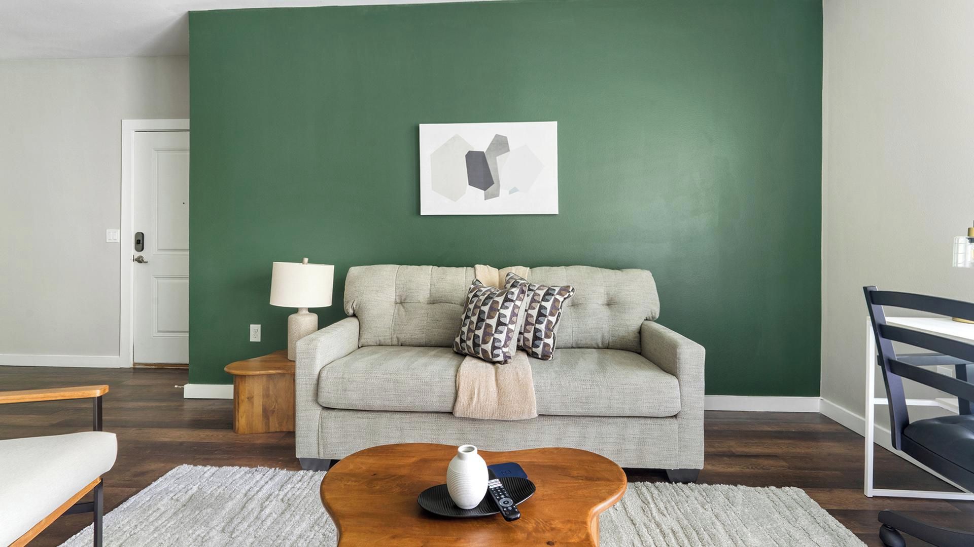 Ein Wohnzimmer mit grüner Wand, einem Sofa, einem Couchtisch, einer Lampe und einem gerahmten Bild.