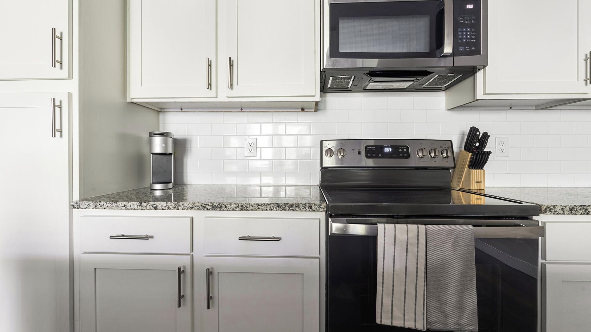 A kitchen with white cabinets, a stainless steel microwave, a stove, and a coffee maker.