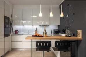 A modern kitchen with white cabinets, a wooden countertop, two black chairs, and pendant lights. - Villa Irma (Malinska)