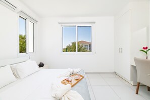 A hotel room with a bed, a window with a view, a wardrobe, and a small table with a tray. - Villa Avra 84 in Protaras (Paralimni)