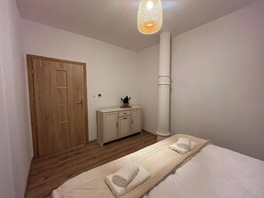 Un dormitorio con puerta de madera, un armario, un alto pilar blanco y una cama con una toalla enrollada.
