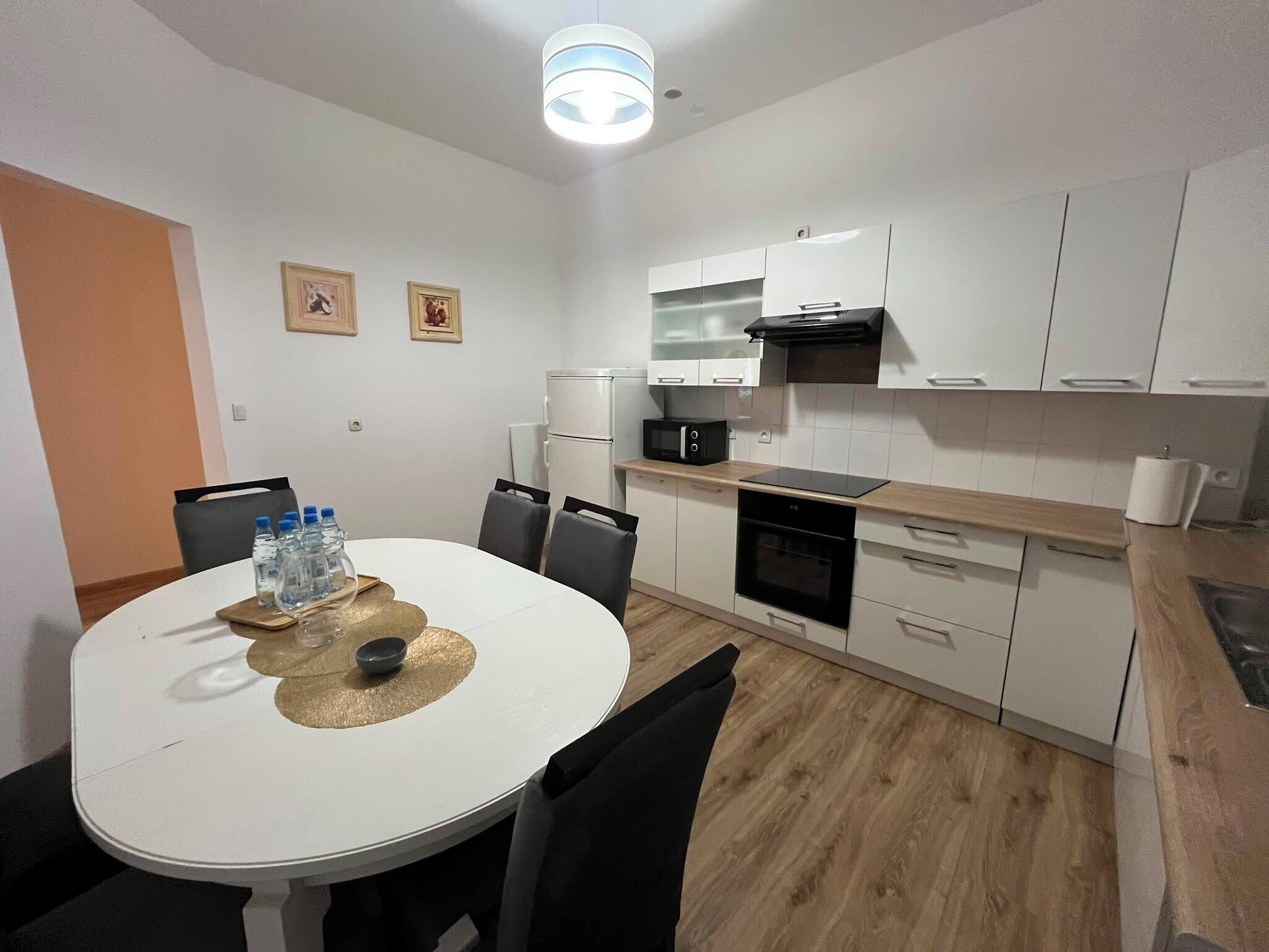 Une cuisine de taille réduite avec des meubles blancs, un four à micro-ondes, une cuisinière et une table à manger avec des chaises.