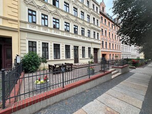 Rivi perinteisiä eurooppalaisia rakennuksia, joissa on parvekkeet, kivetty jalkakäytävä ja metalliaita.
