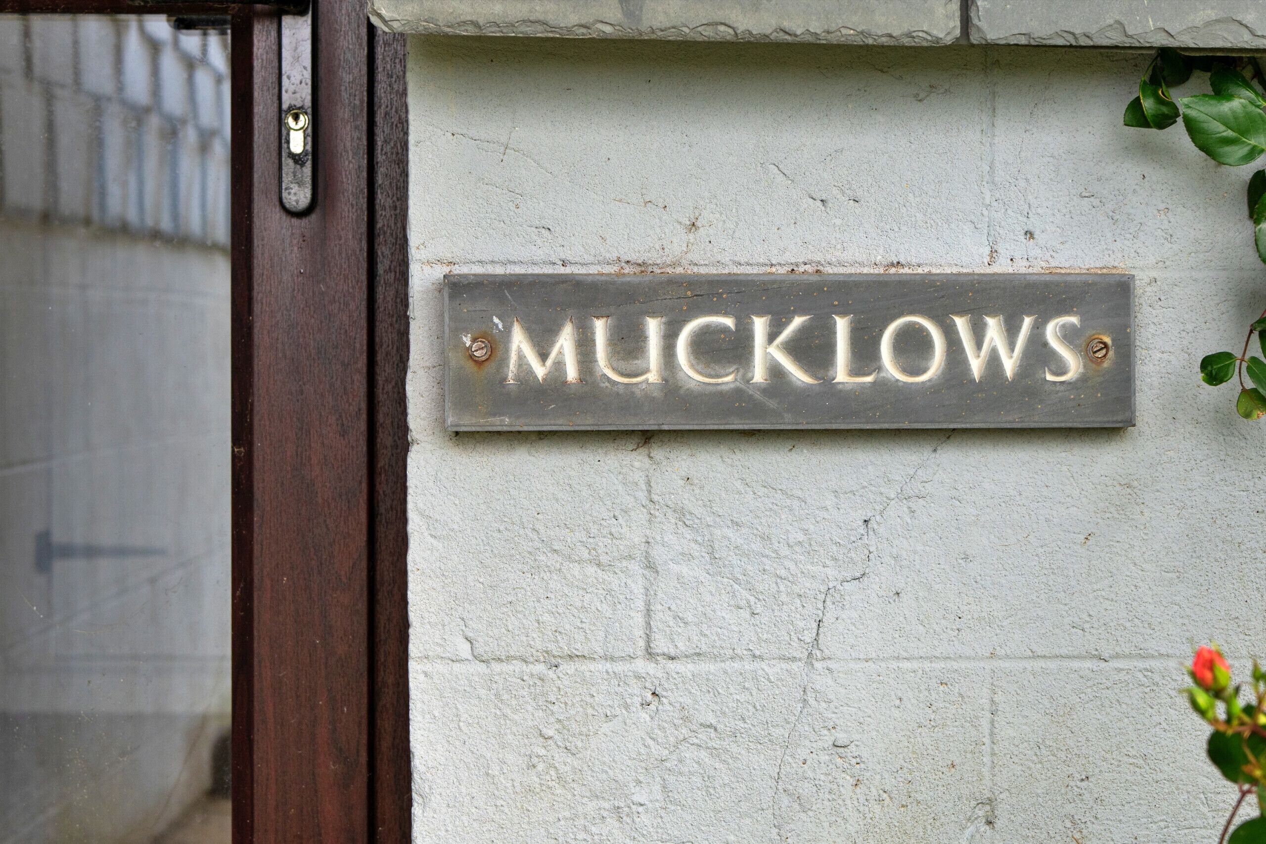 Un letrero de metal con el nombre 'Mucklows' sujeto a una pared blanca.