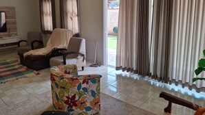 A living room with a sofa, armchairs, a TV, and a large window with curtains.