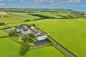 An aerial view of a rural property with a large house, a swimming pool, and expansive green fields. - Squire, Quinceborough Farm (Widemouth Bay)