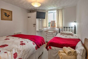 Ein Schlafzimmer mit zwei Betten, einem Fernseher, einem Schminktisch und einem Fenster mit Vorhängen.