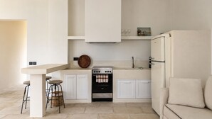 A compact kitchen with a stove, bar stools, a refrigerator, and a sofa. - Lanu sea view apartment (Argostoli)