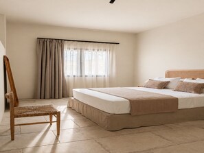 Ein Schlafzimmer mit Bett, Sessel, Fenster mit Vorhängen und Deckenleuchte.