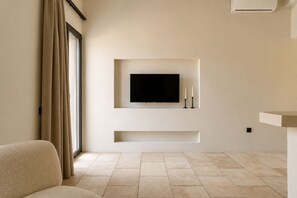 Ein modernes Wohnzimmer mit einem flachbildfernseher an der Wand, einer Couch und einem großen Fenster mit Vorhängen.