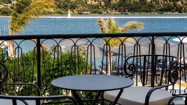 A balcony with a view of a body of water, a sailboat, and a mountainous landscape. - Lanu sea view apartment (Argostoli)