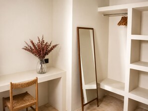 Ein Zimmer mit weißem Schreibtisch, einem Stuhl, einem Spiegel und einem Regal mit Kleiderhaken.