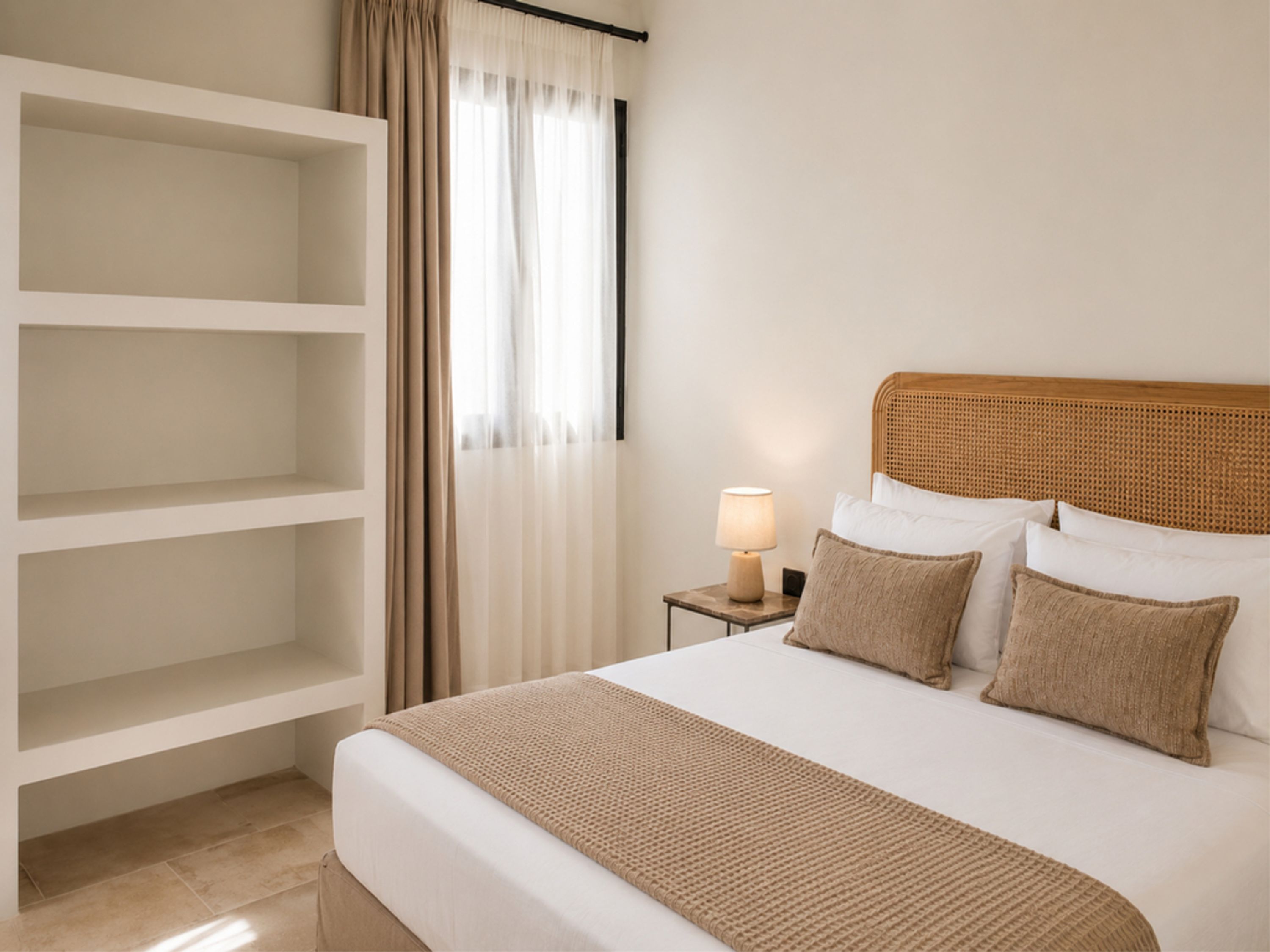 A hotel room with a bed, a bedside table with a lamp, a wardrobe, and a window with curtains.