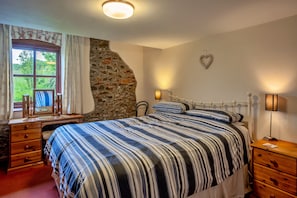 Ein Schlafzimmer mit Stehwand, einem Bett mit gestreifter Bettwäsche, einem Schminktisch und einem Spiegel, sowie einer herzförmigen Dekoration an der Wand.