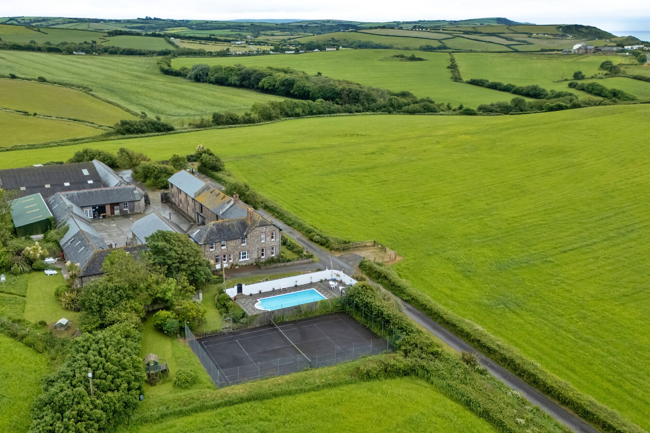 An aerial view of a rural property with a large field, a swimming pool, and a building with multiple rooms.