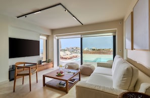 Ein modernes Wohnzimmer mit Sofa, Couchtisch und Fernseher. Große Fenster bieten Blick auf einen Pool und Gebäude.
