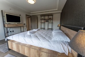 Et soveværelse med en træseng, et fjernsyn monteret på væggen, en hylde med håndklæder og en lampe.