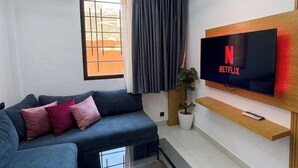 Uma sala de estar moderna com sofá, mesa de centro, TV fixada na parede e um vaso com planta.