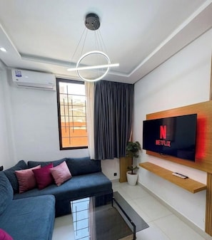 A modern living room with a sofa, a mounted TV displaying Netflix, a ceiling light fixture, and an air conditioning unit. - DOHA MAISON COLLECTION (Marrakesh)