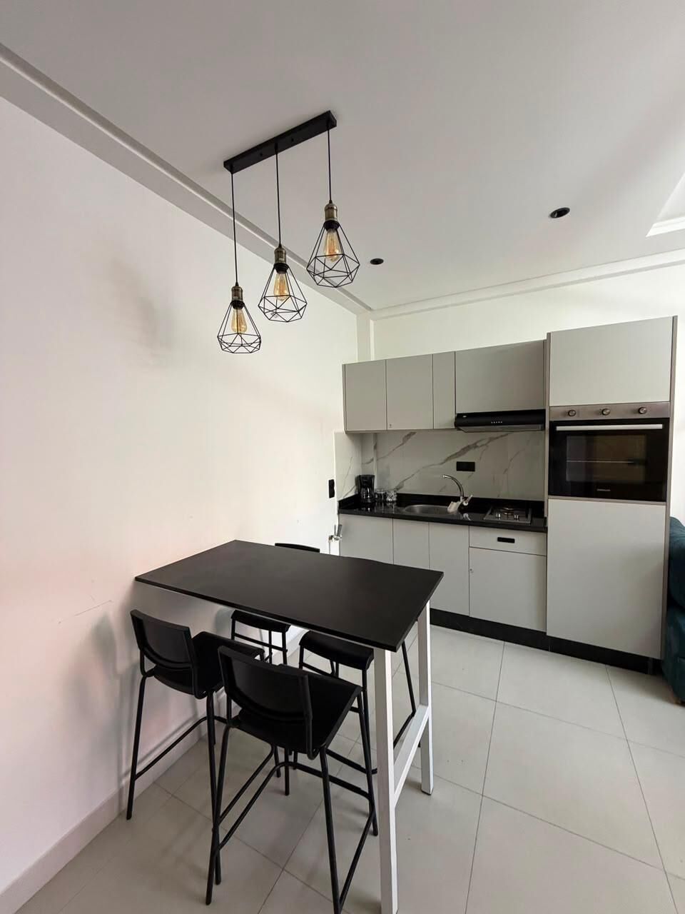 A modern kitchen with white cabinets, a black countertop, and a dining area with a black table and chairs.