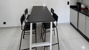 Cozinha moderna com mesa e cadeiras, luminária pendente e parede branca.