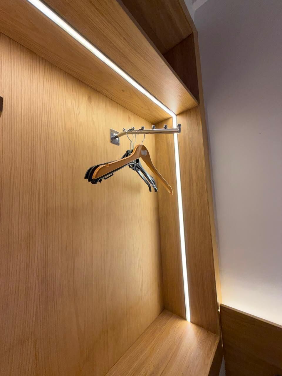 Un armario de madera con barra para colgar y una tira de luz.