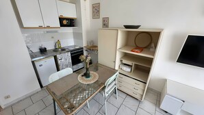 Kompakti keittiö, jossa on mikroaaltouuni, liesi, pesuallas ja pieni jääkaappi. Keittiössä on ruokapöytä ja tuoli, maljakko kukkineen sekä hylly, jossa on kulho ja kirja.