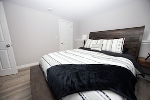 Un dormitorio con cama, mesita de noche, lámpara y una puerta.