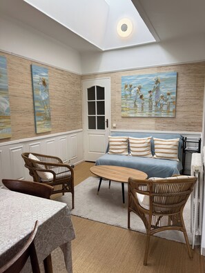 A room with a sofa, two wicker chairs, a small table, a door, and two paintings on the wall. - The Grand Polo • Deauville • 4 bedrooms • Downtown on foot (Deauville)