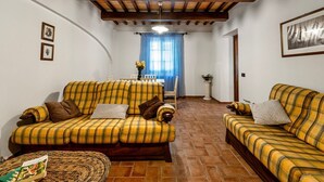 A living room with two yellow plaid sofas, a woven ottoman, and a dining area with a table and chairs. - GuestHost - Il Casale dei Gelsi - Biancospino (San Martino In Campo)