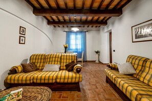 A living room with two yellow plaid sofas, a woven ottoman, and a dining area with a table and chairs. - GuestHost - Il Casale dei Gelsi - Biancospino (San Martino In Campo)