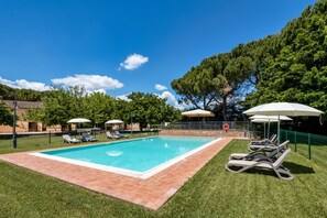 A rectangular swimming pool with a tiled border, surrounded by grass, and shaded by umbrellas. - GuestHost - Il Casale dei Gelsi - Biancospino (San Martino In Campo)
