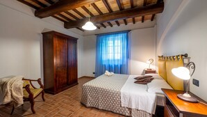 A bedroom with a bed, wooden wardrobe, chair, and a nightstand with a lamp. - GuestHost - Il Casale dei Gelsi - Biancospino (San Martino In Campo)