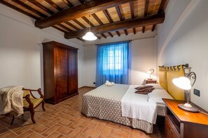 A bedroom with a bed, wooden wardrobe, chair, and a nightstand with a lamp. - GuestHost - Il Casale dei Gelsi - Biancospino (San Martino In Campo)