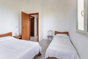 Ein Zimmer mit zwei Betten, einem Sessel, einer Holztür und einem Fenster.