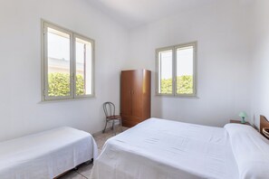 Ein Zimmer mit zwei Betten, einem Kleiderschrank, einem Sessel und Fenstern mit Blick ins Grüne.