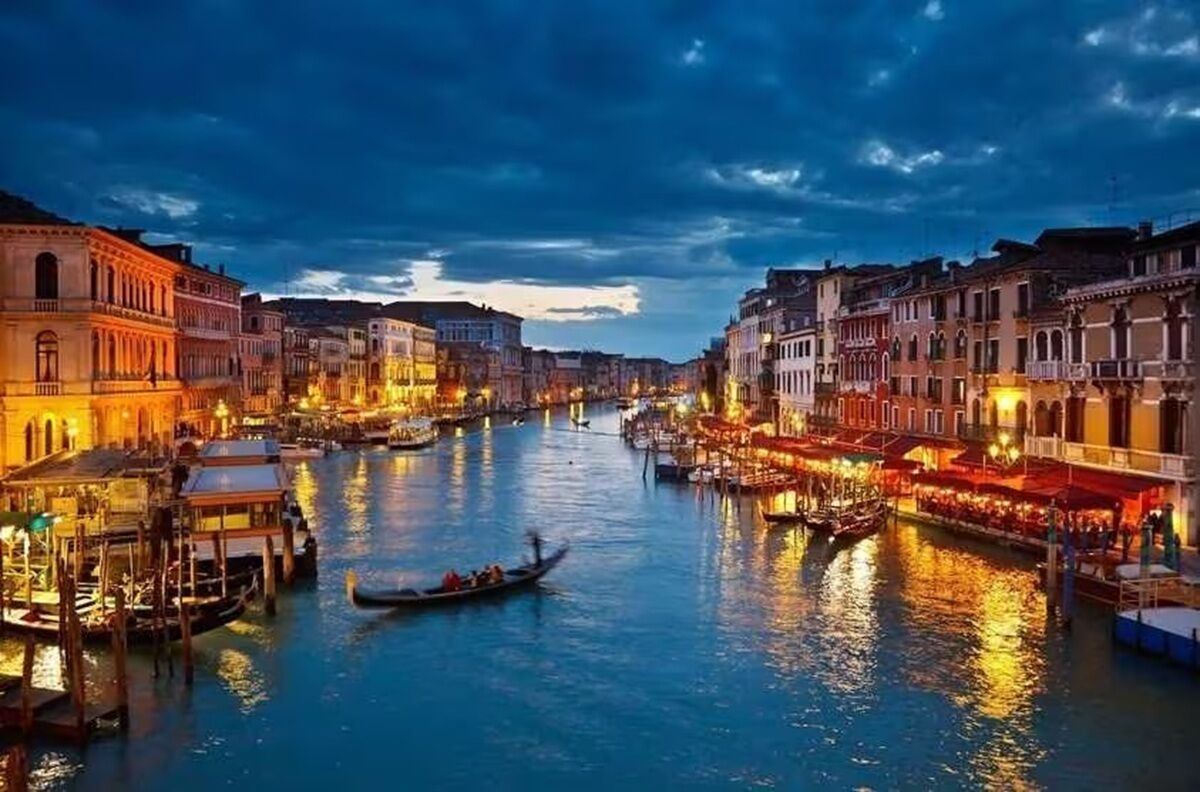 A canal with buildings on either side, gondolas, and a bridge.