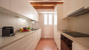 A narrow kitchen with white cabinets, a built-in oven, a microwave, and a window. - Waterfront Venetian Apartment with Canal Views Near Basilica della Salute (Venezia)
