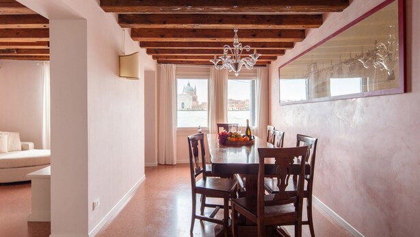 A dining area with a wooden ceiling, a chandelier, a table with chairs, and a window with a view of a building. - Waterfront Venetian Apartment with Canal Views Near Basilica della Salute (Venezia)