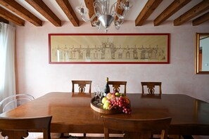 Een eetkamer met een houten tafel, stoelen, een kroonluchter en een kunstwerk in een lijst aan de muur.