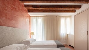 A hotel room with two beds, wooden beams, a wardrobe, and a window with curtains. - Waterfront Venetian Apartment with Canal Views Near Basilica della Salute (Venezia)