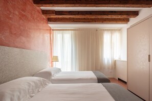 Ein Hotelzimmer mit zwei Betten, Holzbalken, einem Kleiderschrank und einem fenster mit Vorhängen.