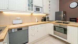 Una cucina moderna con mobili bianchi, un forno a microonde, un tostapane, un lavandino, una stufa e una sveglia appesa al muro.