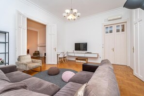Sala de estar com sofá, banquinho, televisão e lustre.