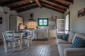 A kitchen with wooden beams, a dining table with chairs, a sofa, and a window with a view. - Atzori Home (Sant'Anna Arresi)