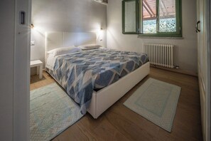 A bedroom with a bed, bedside tables, a radiator, and a window with curtains. - Atzori Home (Sant'Anna Arresi)
