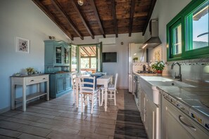 Een keuken met houten vloeren, een eettafel met stoelen, een kast en een raam met groene frames.